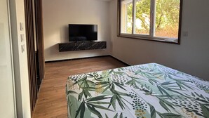 A bedroom with a bed, a TV on a stand, a window with a view of trees, and a wooden floor. - M&R Riviera • Near the beaches • Air Conditioning • Terrace • Modern 5-bedroom apartment • 8 people (La Seyne-sur-Mer)