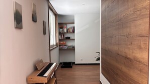A hallway with a piano, wooden flooring, and a bookshelf with books and decorative items. - M&R Riviera • Near the beaches • Air Conditioning • Terrace • Modern 5-bedroom apartment • 8 people (La Seyne-sur-Mer)