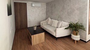 A modern living room with a wooden coffee table, a white sofa, a potted plant, and a wooden door. - M&R Riviera • Near the beaches • Air Conditioning • Terrace • Modern 5-bedroom apartment • 8 people (La Seyne-sur-Mer)