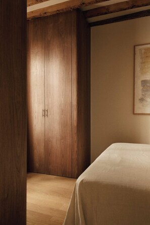 Quarto com guarda-roupa de madeira, cama com colcha branca e um quadro na parede.