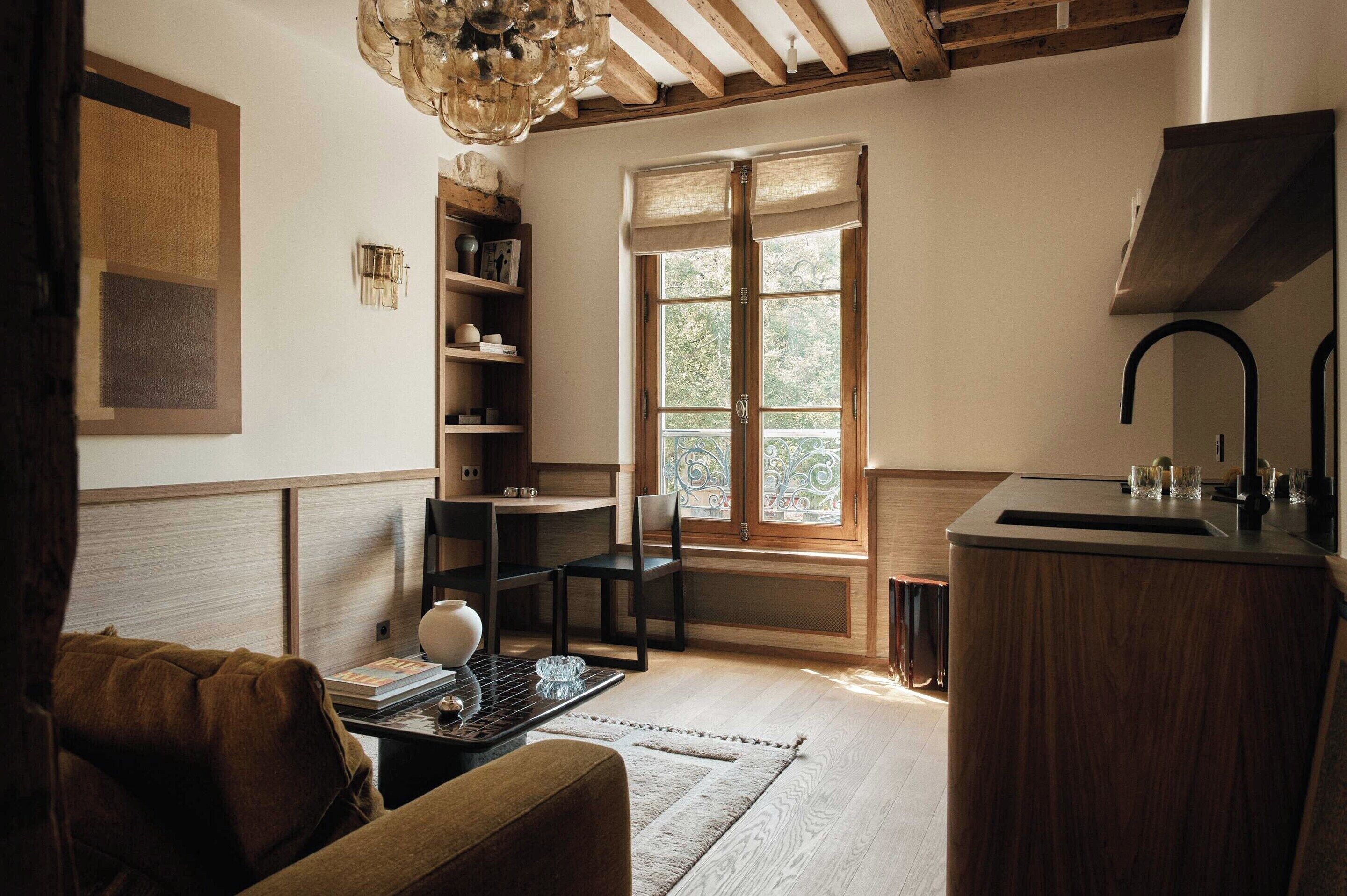 Une pièce avec un plafond en bois, une fenêtre ornée de vitraux, un lavabo, une chaise et une bibliothèque.