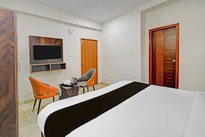 A hotel room with a bed, two chairs, a small table, a TV mounted on the wall, and a wooden door with a geometric pattern.