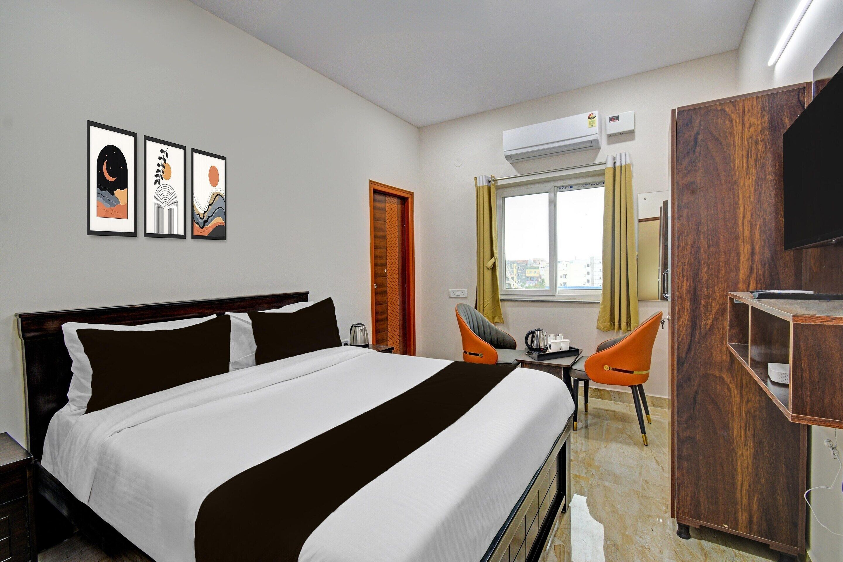 A hotel room with a bed, a desk, two chairs, a wardrobe, and artwork on the wall.