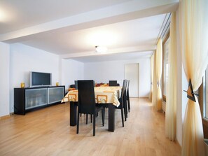 A dining area with a table set for six, a television on a cabinet, and a large window with curtains. - Luegisland Wohnung Salietti Appartement/Fewo, Dusche oder Bad, WC, 8-Bettwohnung by Interhome (Arosa)