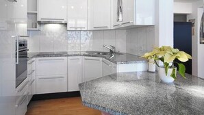 A modern kitchen with white cabinetry, a granite countertop, and a stainless steel range hood. - Luegisland Wohnung Salietti Appartement/Fewo, Dusche oder Bad, WC, 8-Bettwohnung by Interhome (Arosa)
