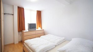 A bedroom with a bed, a TV on a dresser, and a door. - Luegisland Wohnung Salietti Appartement/Fewo, Dusche oder Bad, WC, 8-Bettwohnung by Interhome (Arosa)
