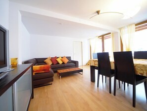 A modern living room with a sofa, ottoman, and a dining area with chairs and a table. - Luegisland Wohnung Salietti Appartement/Fewo, Dusche oder Bad, WC, 8-Bettwohnung by Interhome (Arosa)