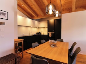 Une cuisine moderne avec des poutres en bois, une table à manger avec des chaises et un luminaire suspendu.