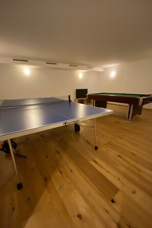 Ein Zimmer mit Tischtennisplatte, Billardtisch und Fernseher.