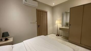 A hotel room with a bed, bedside table, lamp, wardrobe, and a mirror.