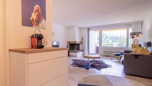 A modern living room with a fireplace, a sofa, a coffee table, and a large window offering a view of the outdoors. - Rothornblick 63 by Arosa Holiday Appartement/Fewo, Dusche, WC Rothornblick 63 by Interhome (Arosa)