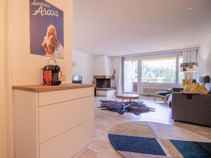 A modern living room with a fireplace, a sofa, a coffee table, and a large window offering a view of the outdoors. - Rothornblick 63 by Arosa Holiday Appartement/Fewo, Dusche, WC Rothornblick 63 by Interhome (Arosa)