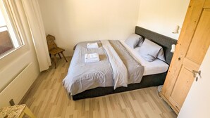 A bedroom with a bed, a wooden wardrobe, a small table, and a window with curtains. - Rothornblick 63 by Arosa Holiday Appartement/Fewo, Dusche, WC Rothornblick 63 by Interhome (Arosa)