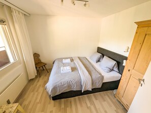 A bedroom with a bed, a wooden wardrobe, a small table, and a window with curtains. - Rothornblick 63 by Arosa Holiday Appartement/Fewo, Dusche, WC Rothornblick 63 by Interhome (Arosa)