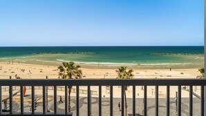 Une vue sur la plage depuis un balcon doté d’une balustrade, avec des palmiers et un ciel dégagé.