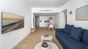 Un salon moderne avec un canapé bleu, une table basse et un tableau représentant une scène de plage.