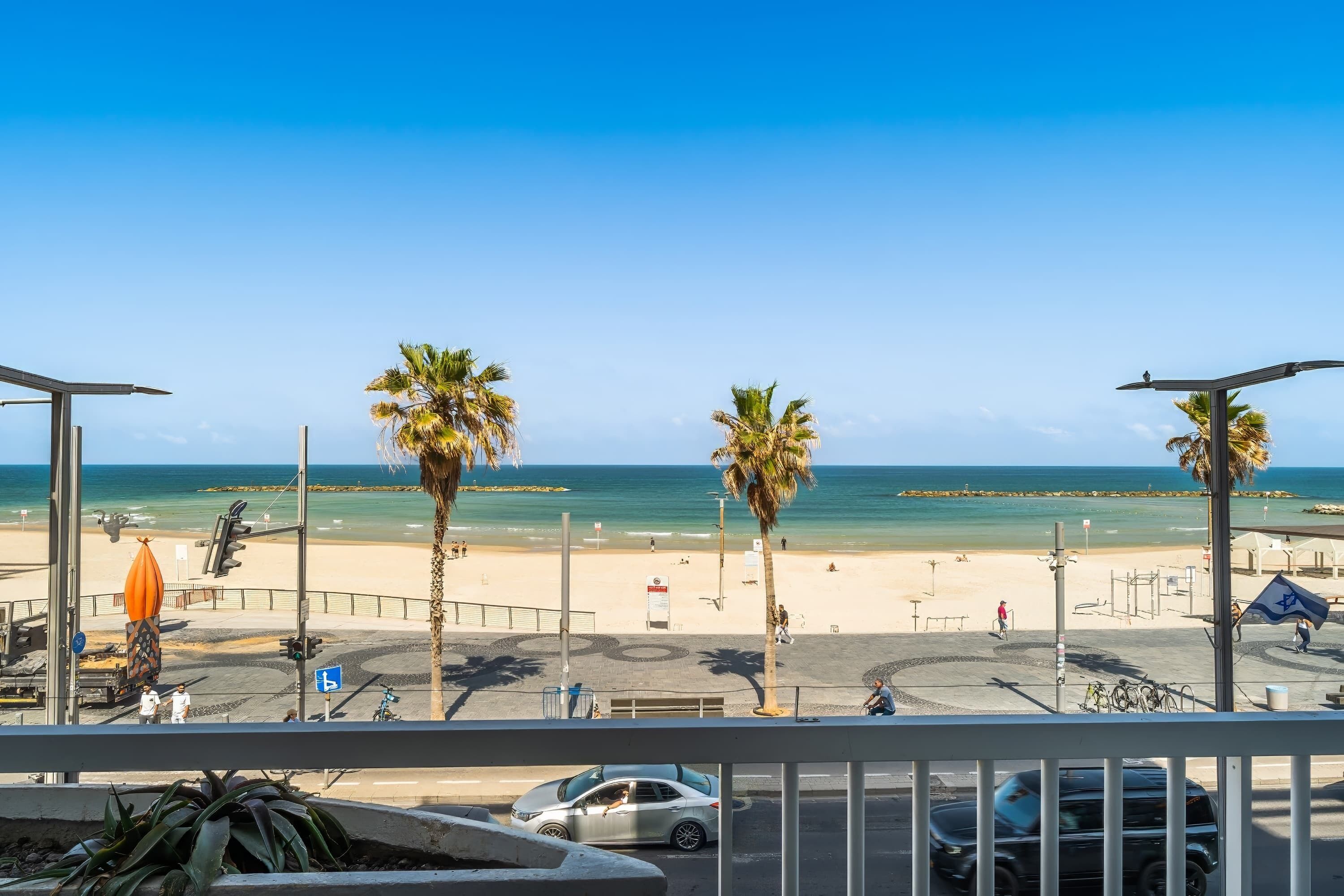A beach view with palm trees, a parking area, and a clear sky.