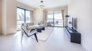 Un salon moderne avec un canapé, des fauteuils, une table basse, un téléviseur et de grandes fenêtres avec des rideaux.