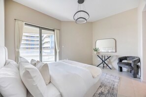 A bedroom with a large bed, a desk with a mirror, a chair, and a view of a building through a window. - Bloomfields 2BR in Ajwan Tower-Saadiyat (Abu Dhabi)