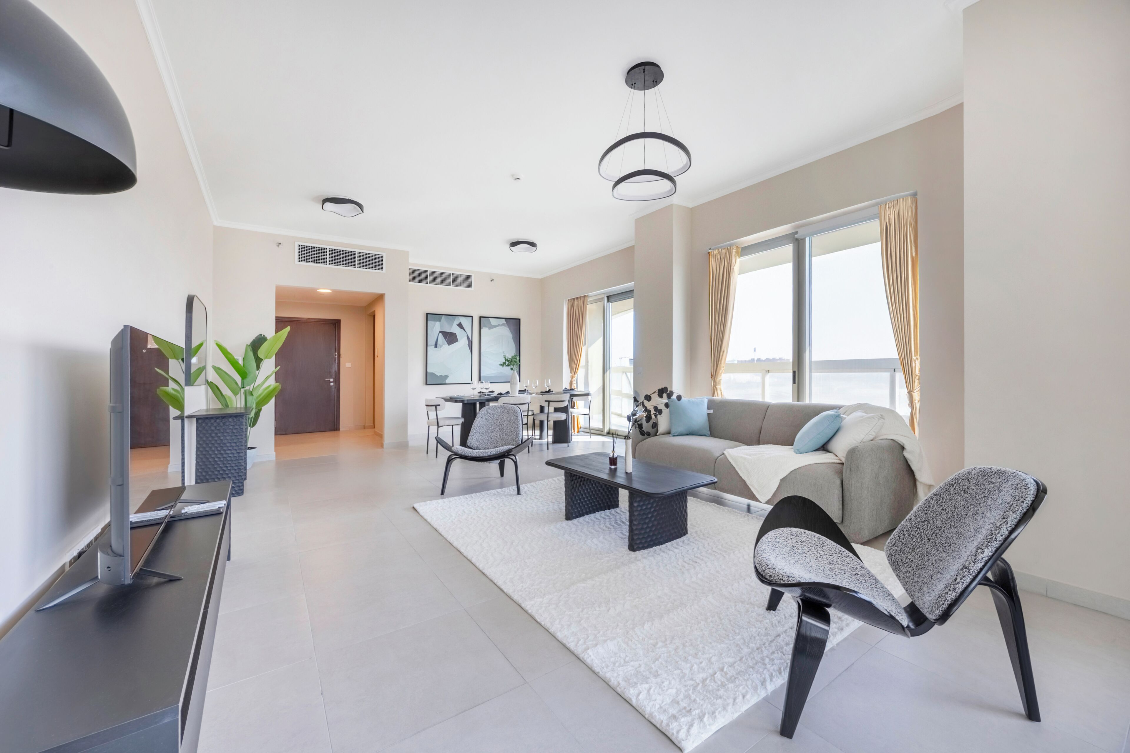 A modern living room with a sofa, chairs, a coffee table, a TV, and a dining area in the background.