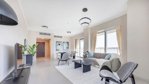Un salon moderne avec un canapé, des fauteuils, une table basse, un téléviseur et, au fond, un coin repas.