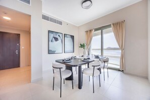 A modern dining room with a large table, six chairs, and a view of the sea through a large window. - Bloomfields 2BR in Ajwan Tower-Saadiyat (Abu Dhabi)