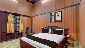 A bedroom with a large bed, wooden walls, a window with curtains, and two framed pictures on the wall. - Deluxe Kallar Vattiyar Waterfalls Munnar (Devikolam)