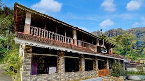 A two-story hotel with a balcony, a signboard, and a view of the surrounding greenery. - Deluxe Kallar Vattiyar Waterfalls Munnar (Devikolam)