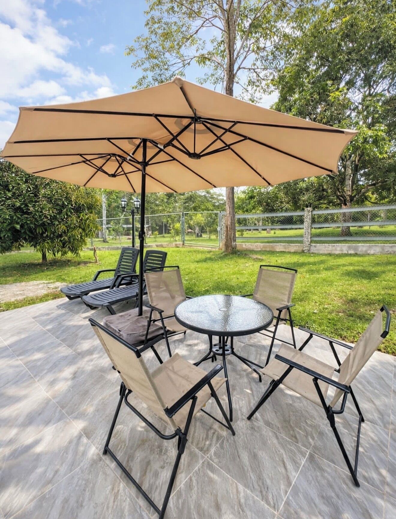 Une terrasse extérieure avec une table ronde et quatre chaises, un grand parasol beige et un sol carrelé.