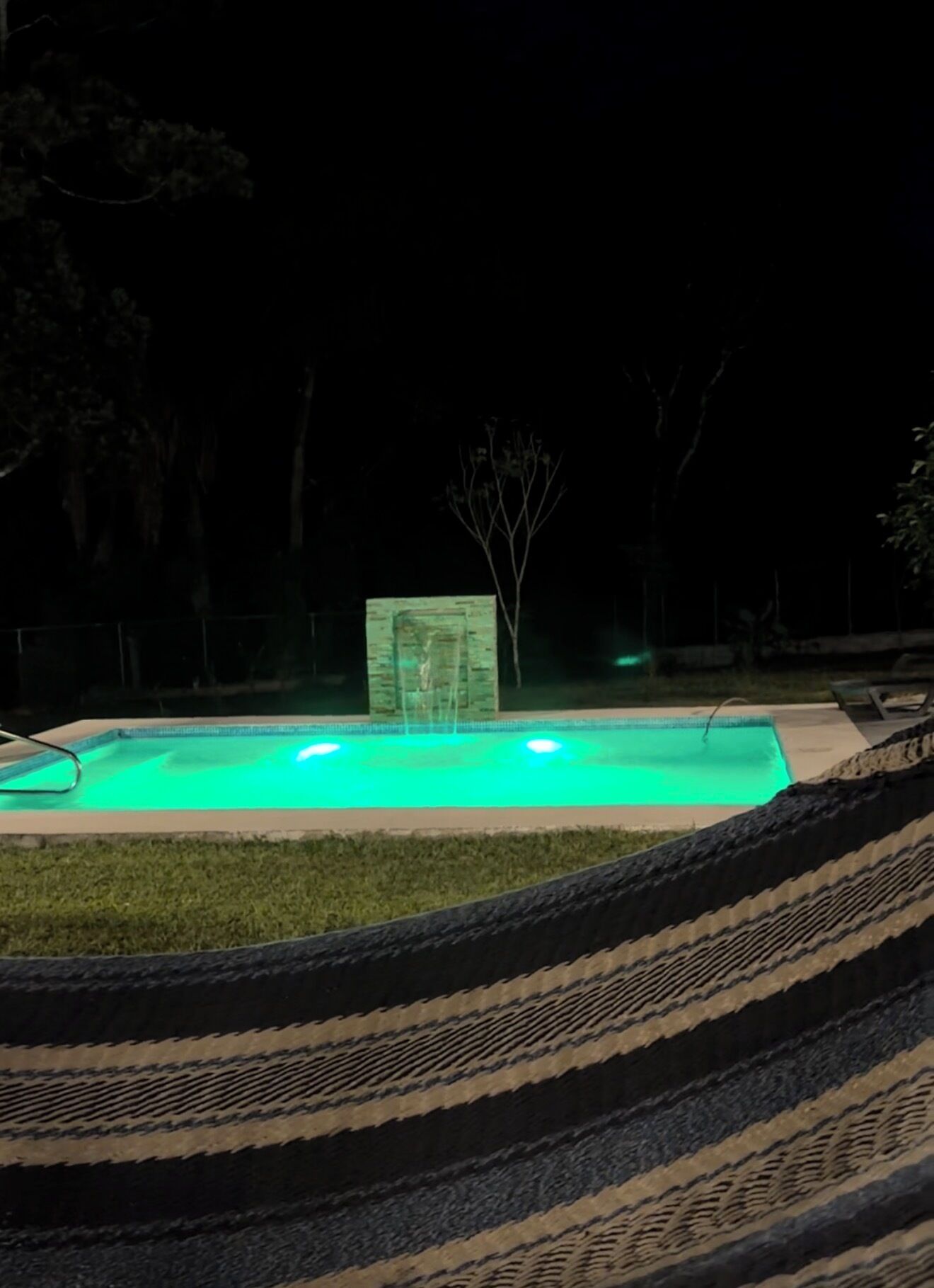 A rectangular swimming pool with a central water feature, surrounded by a dark, textured border.