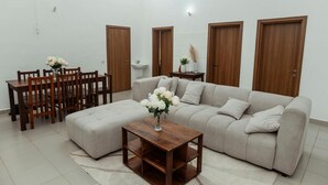 A living room with a sofa, a coffee table, a dining table with chairs, and wooden doors. - Perfect 3-bedroom apartment with AC in welcoming West B Zanzibar (West B, Zanzibar)