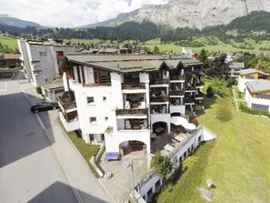 A multi-story building with balconies, a parking area, and a view of mountains in the background. - ARENA Penthouse, (Flims Dorf), 2624 by Interhome (Flims)