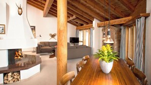 Een ruime woonkamer met een houten eettafel, een open haard en een televisie op de achtergrond.