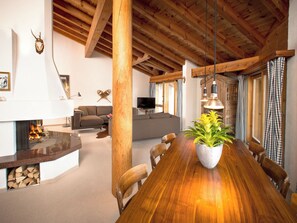 A spacious living area with a wooden dining table, a fireplace, and a television in the background. - ARENA Penthouse, (Flims Dorf), 2624 by Interhome (Flims)