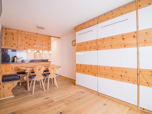 A compact kitchen with wooden cabinets, a dining table with chairs, and a white wardrobe with wooden panels. - Alexandra 611 by Arosa Holiday Appartement/Fewo, Bad, WC, 4-Bettwohnung by Interhome (Arosa)