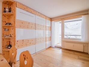 Ein Zimmer mit Holzwänden, einem großen Fenster mit Bergblick, einem Holzstuhl und einem Tisch.