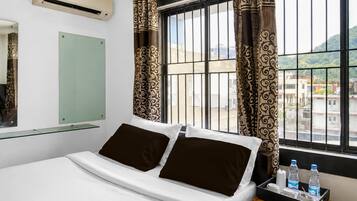 Una habitación de hotel con una cama, una mesita de noche con botellas de agua, un espejo y cortinas.