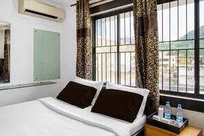 A hotel room with a bed, a bedside table with water bottles, a mirror, and curtains. - Hotel O Bhangagarh (Guwahati)