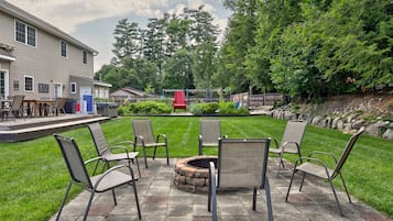 Une terrasse avec des chaises, un foyer extérieur et une pelouse, avec une maison en arrière-plan.