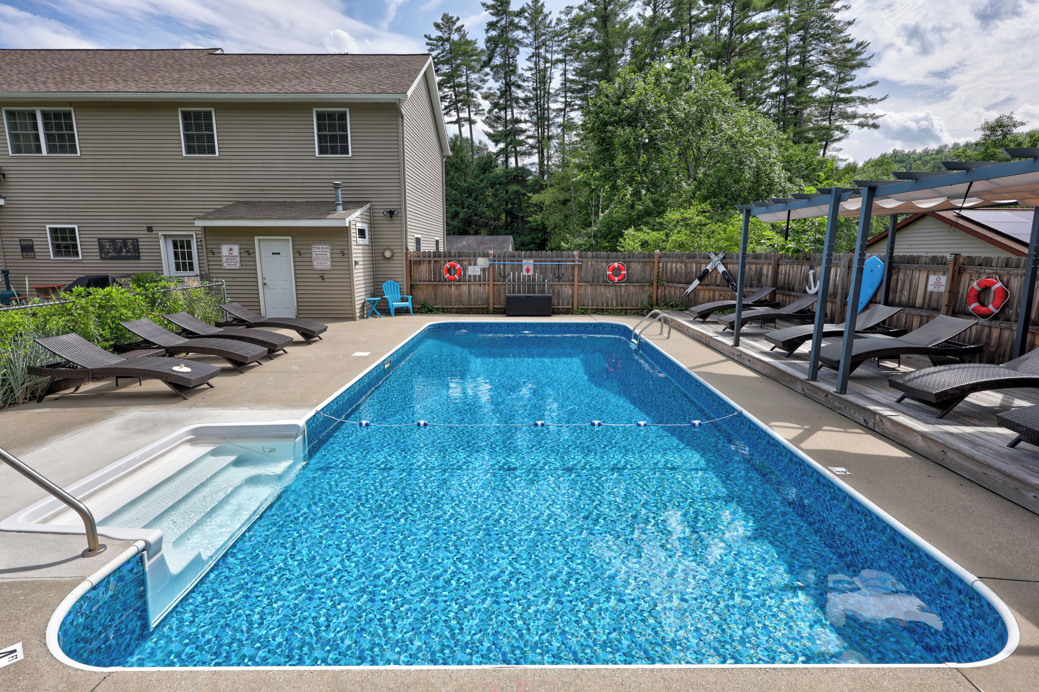 Une piscine rectangulaire dotée d’une terrasse en bois, de chaises longues et d’un espace salon abrité.