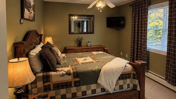 Een slaapkamer met een bed, nachtkastje, lamp, spiegel, plafondventilator en een raam met gordijnen.