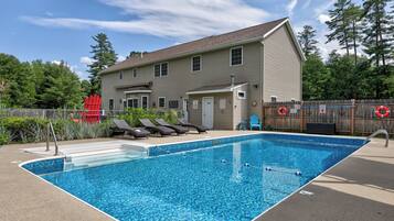 A rectangular swimming pool with a metal ladder, surrounded by a wooden fence.