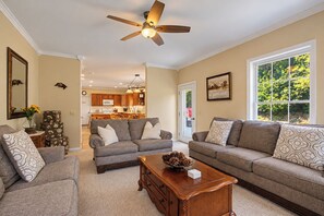 A living room with a ceiling fan, two sofas, a coffee table, and a view of the kitchen and outdoors.