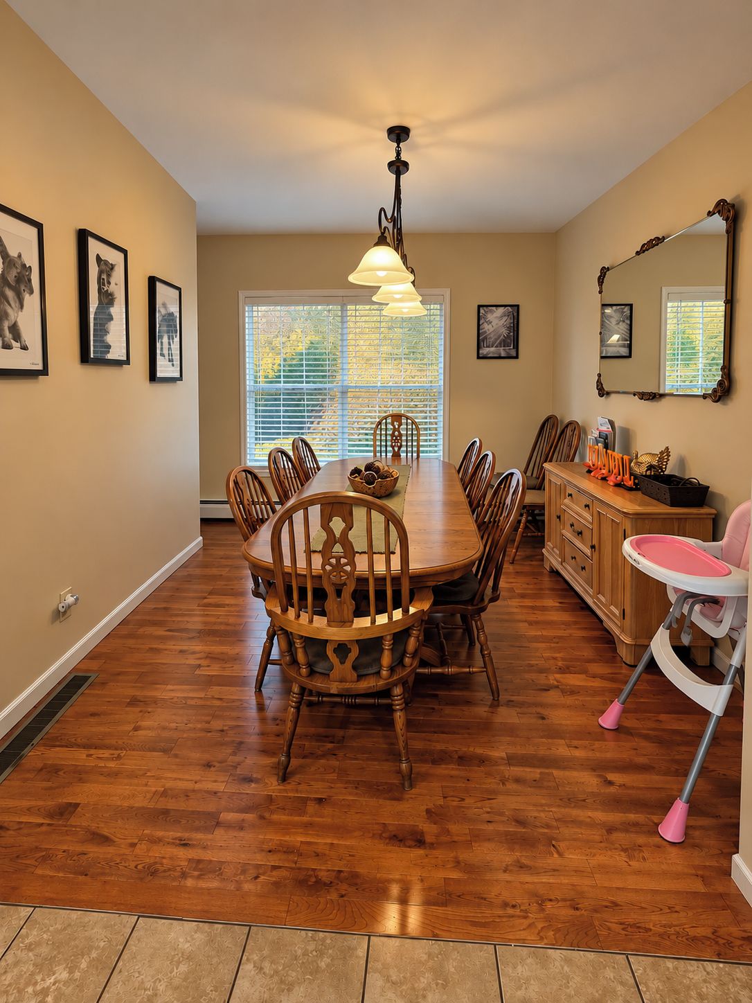 A dining room with a wooden table and chairs, a chandelier, and a window with blinds.