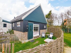 A house with a sloped roof, a front door, and a small front yard with a wooden fence and a table with chairs. - Cosy Suite in Village of Callanstoog (Callantsoog)
