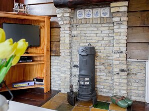 A room with a brick wall, a wooden shelf with books, a television, and a black stove. - Cosy Suite in Village of Callanstoog (Callantsoog)