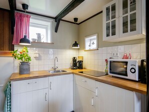 A kitchen with white cabinets, a sink, a coffee maker, a microwave, and a window with a red curtain. - Cosy Suite in Village of Callanstoog (Callantsoog)