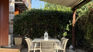 Eine Terrasse mit Tisch, Stühlen, einer Laterne und einem Hecken im Hintergrund.