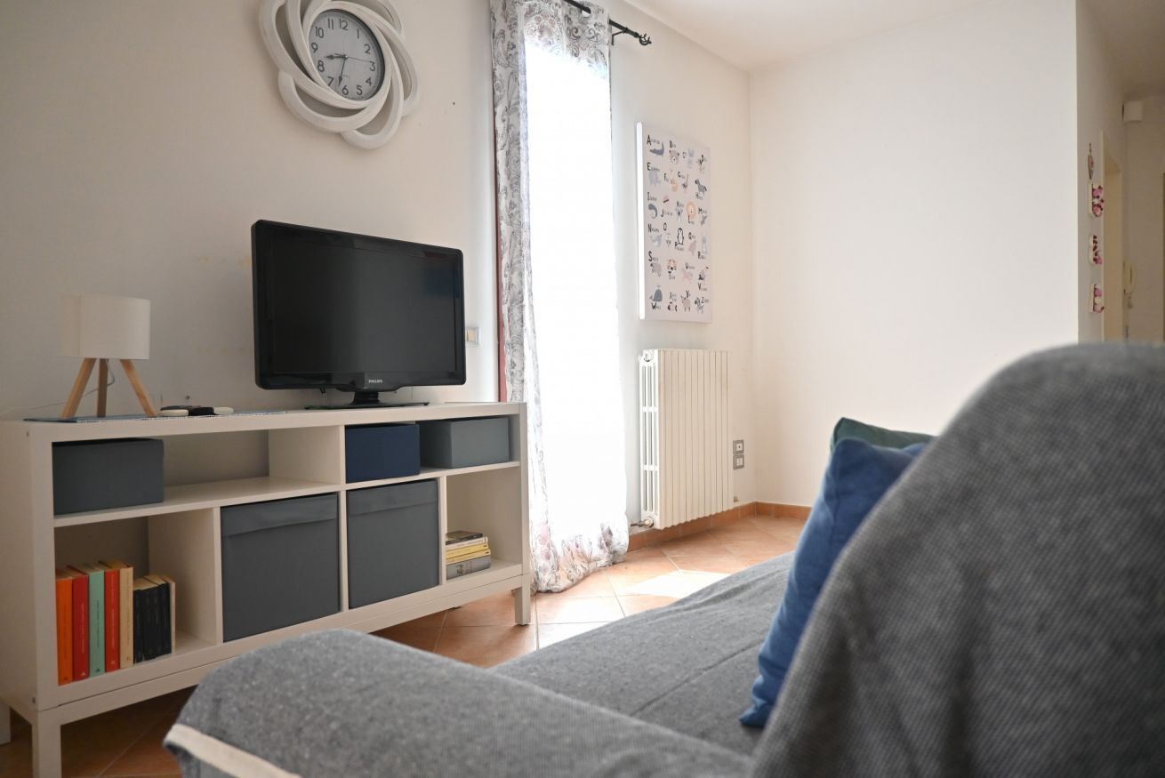 A living room with a television on a stand, a bookshelf, a radiator, and a window with curtains.