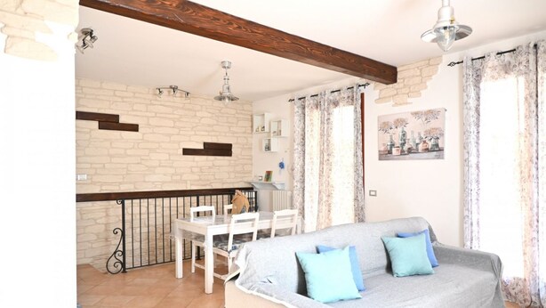 Ein Wohnzimmer mit einer Couch, einem Esstisch mit Stühlen, einer Küchenzeile und einem Balkon mit Geländer.